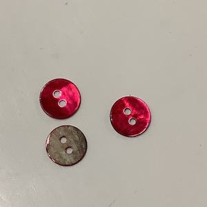 Könnte beinhalten: Drei Zwei-Loch-Knöpfe mit einem pinkfarbenen, irisierenden Finish.