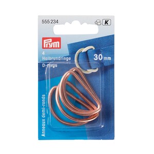 May include: Package of four 30 mm copper D-rings. The package is labeled with the Prym brand name and the text "Halbrundringe D-Ringe" in German and "Anneaux demi-ronds" in French.