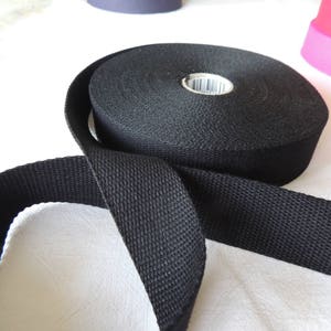 May include: Black cotton webbing strap, approximately 1 inch wide, with a woven texture. The strap is folded in half and the ends are overlapping.