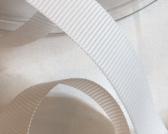 May include: White grosgrain ribbon with a ribbed texture. The ribbon is folded and arranged on a white surface.