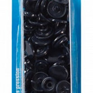 Könnte beinhalten: Eine Packung mit 30 schwarzen "Color Snaps" Druckknöpfen, jeweils mit einem Durchmesser von 12,4 mm. Die Verpackung ist aus transparentem Kunststoff mit einem blau-weißen Etikett. Das Etikett enthält das Prym-Logo und Text in mehreren Sprachen.