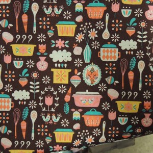 May include: A brown fabric with a repeating pattern of kitchen-themed illustrations. The pattern includes pots, pans, whisks, carrots, birds, and other kitchen-related items. The illustrations are in shades of orange, yellow, blue, green, and white.