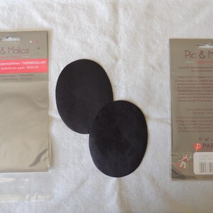 Peut inclure: Deux écussons noirs ovales pour coudes ou genoux, à côté de deux paquets de patchs thermocollants Pic & Malice. Les paquets sont argentés et marron, avec du texte et des illustrations. Les patchs servent à réparer ou personnaliser des vêtements.