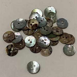 Peut inclure: Un tas de boutons nacrés irisés avec un motif marbré brun et vert. Les boutons ont deux trous et sont disposés de manière aléatoire.