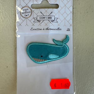 Peut inclure: Un écusson thermocollant en forme de baleine turquoise. Il présente des détails brodés, dont une bouche souriante et une queue incurvée. L'emballage transparent porte les inscriptions "COM' IDÉE" et "Ecusson à thermocoller".