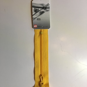 May include: A bright yellow zipper with a matching pull tab, measuring 10 cm in length. The zipper is attached to a white tag with the text "Z51" and the brand "Eclair Prym". The tag also indicates a length of 118.