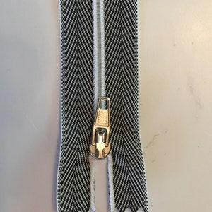 May include: A black and white zipper with a silver slider. The zipper tape has a herringbone pattern.