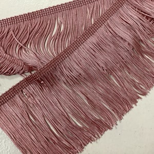 Op de afbeelding: Een close-up van een roze franje trim. De franje is gemaakt van dunne strengen stof en is ongeveer 2,5 cm lang.