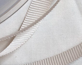 May include: Close-up of white satin ribbon with a textured, ribbed surface. The ribbon is folded and layered, creating a soft, elegant look.