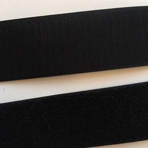 Op de afbeelding: Twee stroken zwart klittenband. De bovenste strook is de haakzijde en de onderste strook is de luszijde.