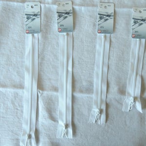 May include: Four white zippers of varying lengths are displayed against a white fabric background. Each zipper has a silver-colored pull and is attached to a cardboard tag with printed text. The zippers are arranged vertically, showcasing their construction and design.