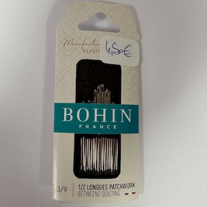 Peut inclure: Un paquet d'aiguilles à quilter Bohin France. L'emballage est blanc avec une étiquette turquoise et noire. L'étiquette indique "BOHIN FRANCE" et "1/2 Longues Patchwork Between Quilting". Le paquet porte également la mention "Manufacture Depuis".