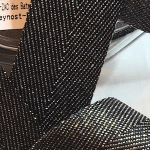 May include: Close-up of black fabric with a chevron pattern and a subtle shimmer. The fabric is made of a fine, tightly woven material.