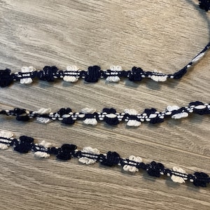 Peut inclure: Garniture blanche et bleu marine avec un motif floral. La garniture est en tissu tissé et a un aspect délicat et féminin.