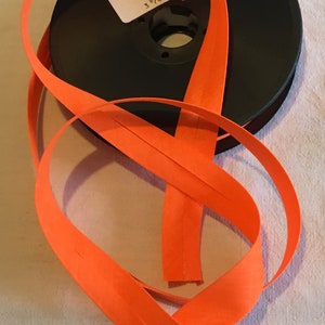 May include: A spool of 20 mm wide orange bias tape. The label reads "Biais fluorescent 25 cm", "50% coton 50% polyester", and has a washing instruction symbol. The barcode is 3 700777 233133.