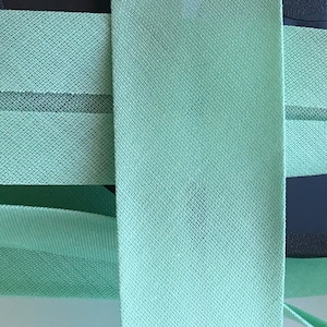 Puede incluir: Dos piezas de tela elástica verde claro con tejido texturizado. La tela está doblada y apilada una encima de la otra.