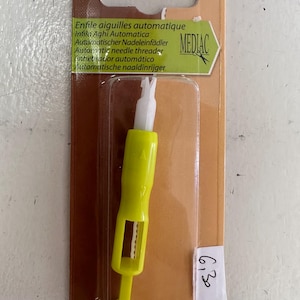 May include: A yellow and white automatic needle threader in a clear plastic package. The package has text in multiple languages, including "Automatic needle threader" and "MEDIAC". The packaging is brown and green.
