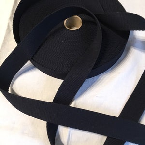 May include: A roll of black webbing strap, a type of heavy-duty fabric used for making straps, belts, and other items.