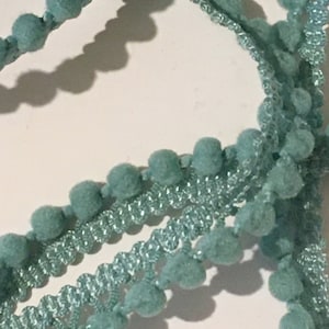 Puede incluir: Una cinta de pompones azul turquesa con una doble fila de pompones. La cinta está hecha de un material suave y peludo y tiene un acabado delicado y brillante.