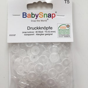 May include: A pack of 30 clear plastic snap buttons, labelled "BabySnap" and "Druckknöpfe (snap buttons) 30 Stück - T5 (12.4mm) transparent. Allergiker geeignet".