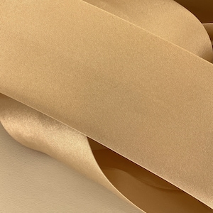 May include: A close-up of a roll of gold satin ribbon. The ribbon is smooth and shiny, with a subtle sheen.