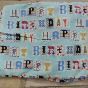 Op de afbeelding: Een blauwe stof met een herhalend patroon van kleurrijke vierkanten met de tekst "Happy Birthday".
