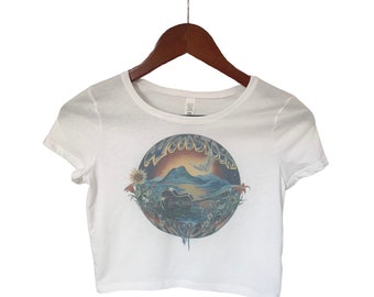 May include: White cropped t-shirt with a colorful graphic of a sunset scene with a mountain, a guitar, and the word "Woodstock" in a circle.