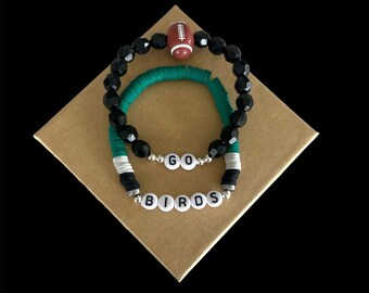 May include: Two bracelets with black and green beads, one with a football charm and the other with the words "GO BIRDS" in white letters.