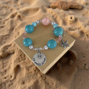 May include: Turquoise and pink beaded bracelet with a silver charm that says "my happy place" and the initials "WB". The bracelet also has a silver starfish charm.