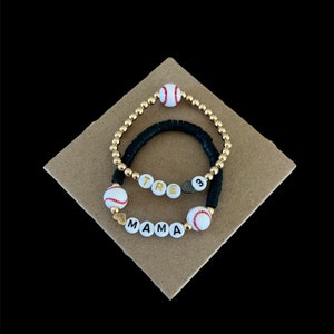 May include: Two black beaded bracelets with gold beads and white baseball charms. One bracelet spells "MAMA" and the other spells "TRE" with a number "3" charm.