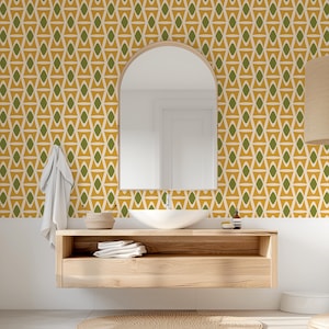 May include: A bathroom with a mid-century modern design. The focal point is a wooden vanity with a white sink and a large arched mirror. The wallpaper features a geometric pattern in gold, olive green, and cream. A white towel hangs on the wall.