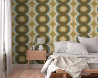 May include: Wallpaper featuring a repeating geometric pattern of concentric circles in shades of olive green, teal, and cream. The design covers the wall behind a wooden nightstand with a white lamp and a bed with white bedding and pillows.