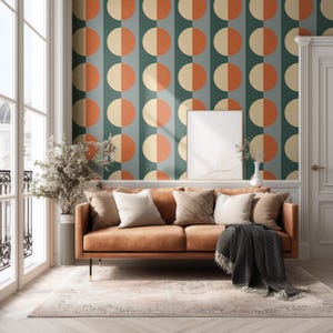 May include: A living room scene featuring a brown leather sofa, cushions, and a patterned rug. The wall is decorated with a retro design of orange and cream-coloured half-circles on a teal backdrop. A blank framed picture hangs on the wall.