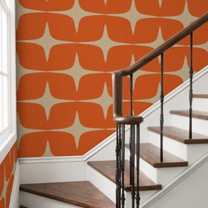 May include: A staircase with a mid-century modern design. The wall features orange and beige wallpaper with a repeating starburst pattern. The wooden handrail and steps are a dark brown, and the risers are white.
