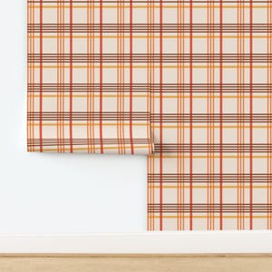 Pode incluir: Rolo de papel de parede com um padrão xadrez em tons de creme, laranja, vermelho e castanho. O design apresenta linhas verticais e horizontais que se cruzam, criando uma aparência de grade. O rolo está parcialmente desenrolado, revelando o padrão.