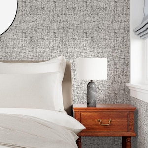 May include: A bedroom scene featuring a bed with white bedding, a wooden nightstand, and a lamp with a white shade. The lamp has a gray marble base. The wall is covered in a textured gray and white wallpaper.