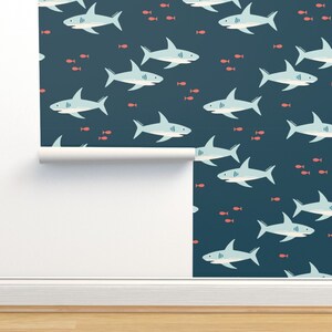 Op de afbeelding: Een naadloos patroon met lichtblauwe haaien die zwemmen in een donkerblauwe oceaan met kleine rode vissen. Het patroon is perfect voor een kinderkamer of een babykamer.