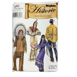 May include: Simplicity Historic Native American Dress sewing pattern envelope 5446. The white package features illustrations of four outfits: a tan fringed tunic with a headdress, a tan dress with fringe, a purple dress, and a yellow jacket with pants.