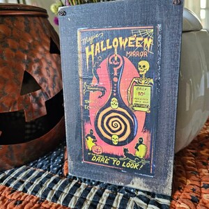 Può includere: Un'insegna a specchio di Halloween in stile vintage con una cornice nera. L'insegna presenta una grafica colorata con la scritta "Magic Halloween Mirror" e uno scheletro. L'insegna include anche la scritta "Dare to Look!"