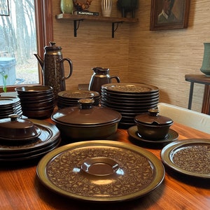 May include: A set of brown and green ceramic dinnerware with a floral pattern. The set includes plates, bowls, a serving dish, and a creamer.