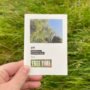 May include: A white card with a picture of a tree and blue sky. The card reads "an ESSENTIAL PACKING LIST for TREE TIME". The card is held in front of a background of green grass.