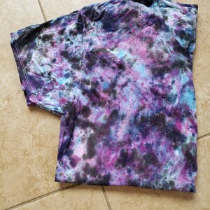 May include: A tie-dye t-shirt with a swirling pattern of black, purple, blue, and white.