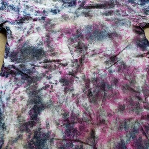 May include: A tie-dye t-shirt with a V-neck in shades of pink, blue, white, and gray.