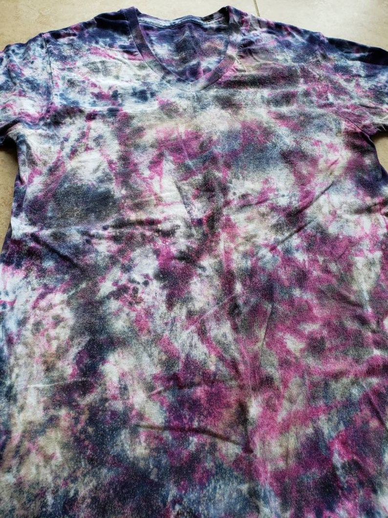 May include: A tie-dye t-shirt with a V-neck in shades of pink, blue, white, and gray.