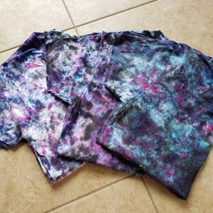 May include: Three tie-dye t-shirts in shades of blue, purple, and white with a galaxy-like pattern.