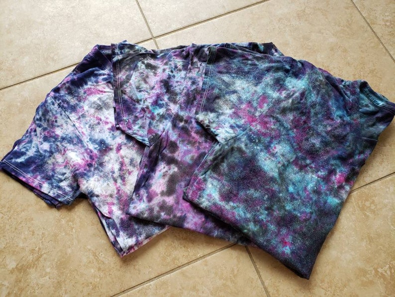 May include: Three tie-dye t-shirts in shades of blue, purple, and white with a galaxy-like pattern.