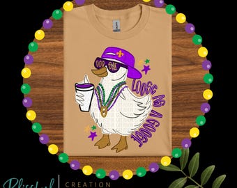 May include: Tan t-shirt featuring a cartoon goose wearing sunglasses, a purple hat, and a beaded necklace, holding a drink. The text "Loose as a Goose" is printed on the shirt. The shirt is surrounded by Mardi Gras beads.