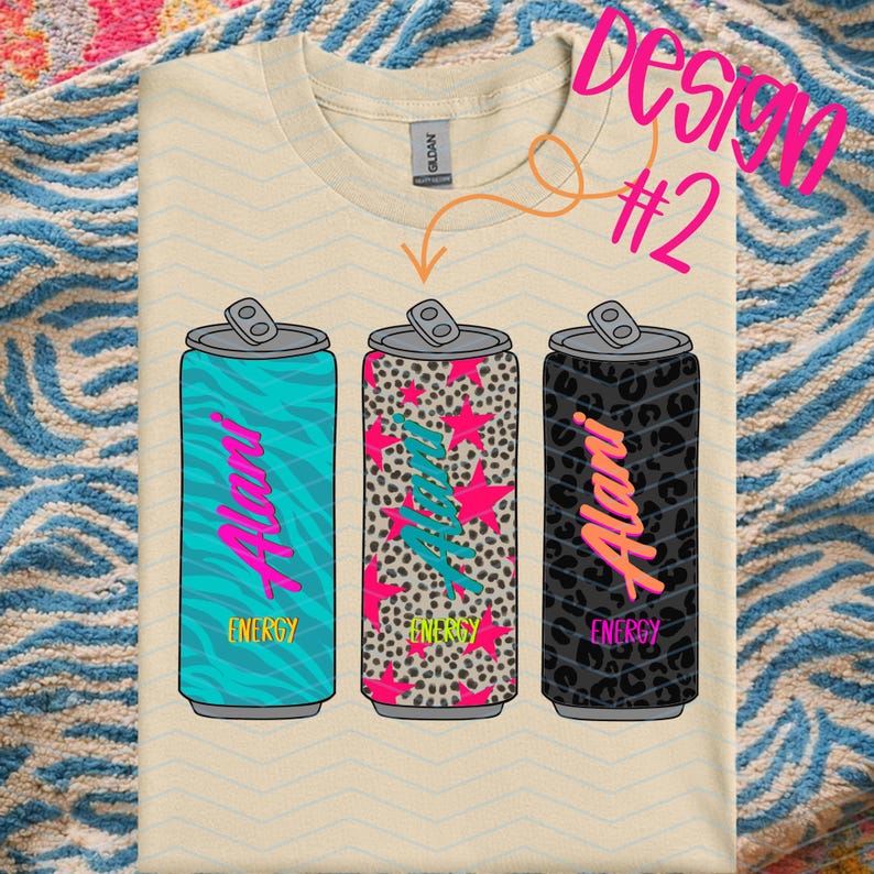May include: Cream-colored t-shirt featuring three stylized energy drink cans. Each can has a different design: teal zebra print, pink star and leopard print, and black leopard print. The word "Alani" is written on each can in a neon pink script, with the word "Energy" below.