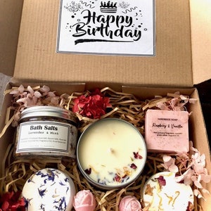 Op de afbeelding: Een cadeaudoos gevuld met bad- en lichaamsverzorgingsproducten. De doos bevat een kaars, badzout, badbommen en zeep. Het badzout is gelabeld met "Bath Salts Lavender & Mint". De zeep is gelabeld met "Handmade Soap Raspberry & Vanilla". De doos is versierd met een kaartje met "Happy Birthday".
