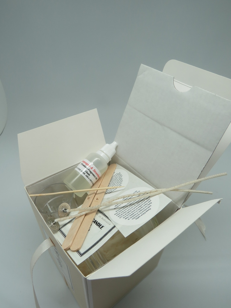 May include: A white box with a clear glass jar, two wooden sticks, a small bottle of liquid, and white wicks. The box is open and the contents are visible. The jar has a label that says "CANDLE" and "Made in Australia". The bottle has a label that says "Soy Wax & Soy Fragrance Oil".